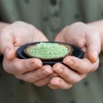 Person holding a plate of green powder used for raw vegan foods