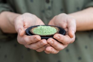 Person holding a plate of green powder used for raw vegan foods