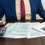 Man fillilng and accounting finance document tax form 1040 with calcualtor. Time for tax.