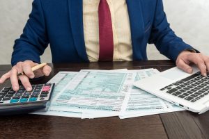 Man fillilng and accounting finance document tax form 1040 with calcualtor. Time for tax.